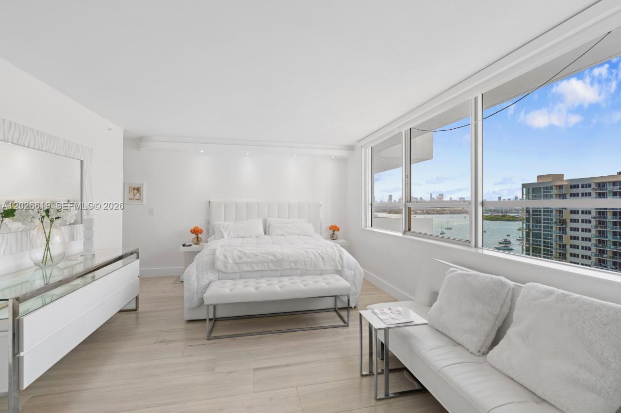 A bright bedroom features a white bed, a sofa, and large windows overlooking the water — 1500 Bay Rd # 1268S, Miami Beach FL 33139, MIAMI BEACH, FL