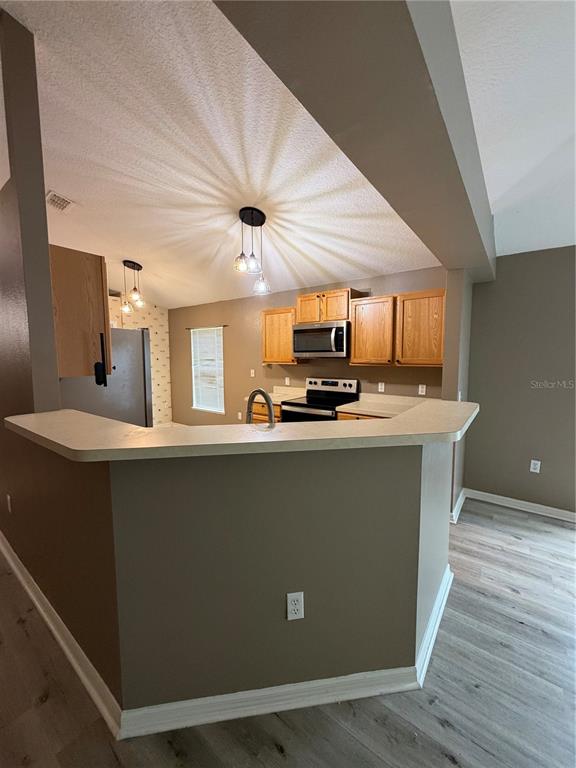 A kitchen with wood cabinets, stainless steel appliances, and a peninsula counter overlooks a room — 5539 SYCAMORE CANYON DRIVE, KISSIMMEE, FL