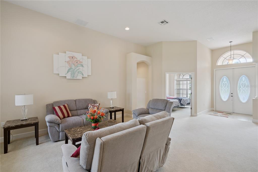 A living room features light carpet, neutral walls, a grey sofa set, and an arched entryway — 3700 DUNOON COURT, APOPKA, FL