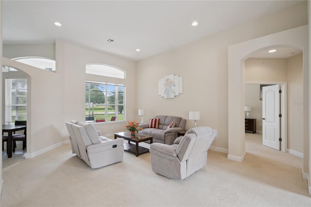 A living room with beige carpet, light-colored walls, a sofa, two recliners, and large windows — 3700 DUNOON COURT, APOPKA, FL