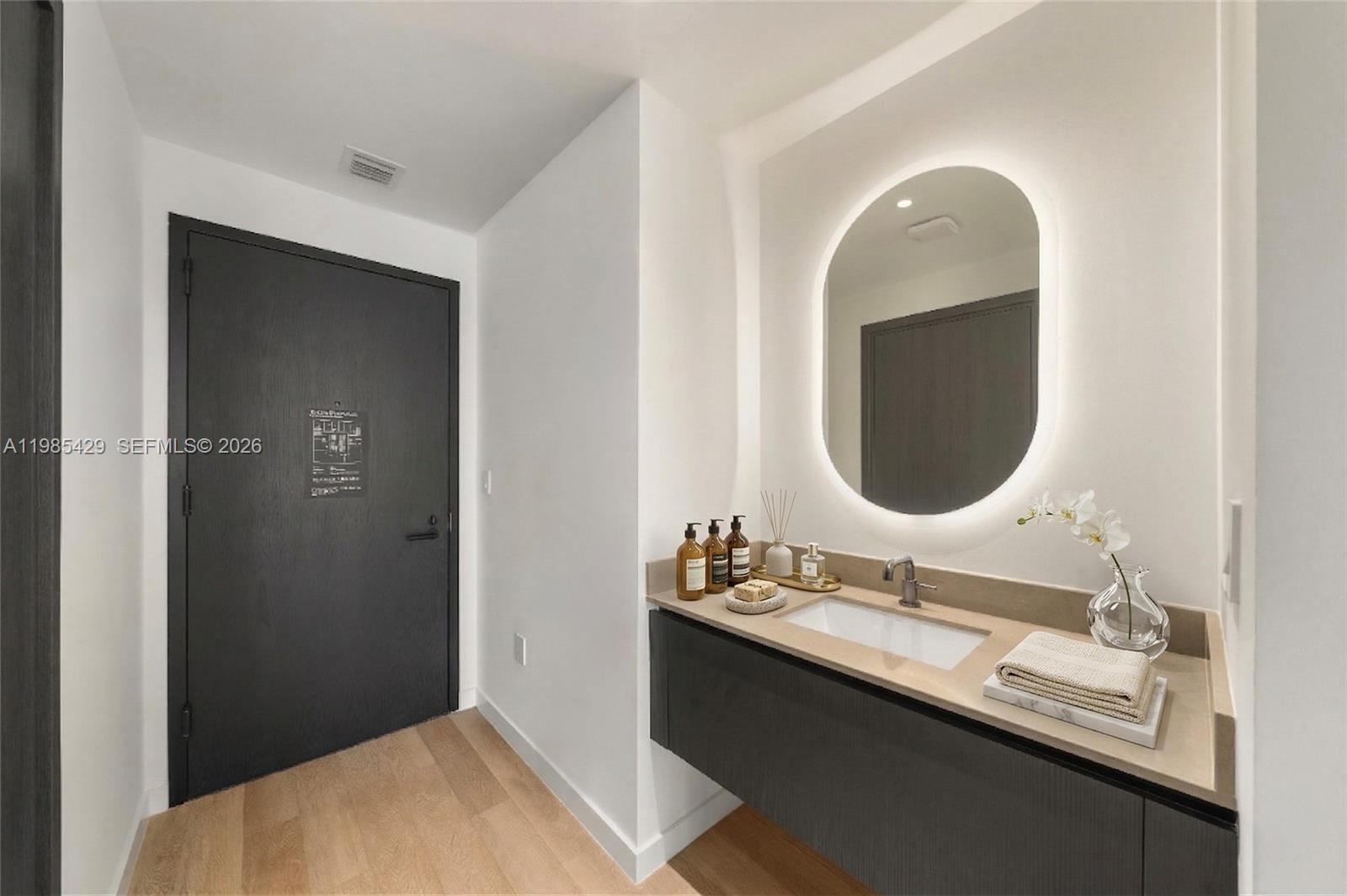 A modern bathroom features a floating vanity, an oval backlit mirror, and a dark door — 20 NE 11 ST # 2306B, Miami FL 33132, MIAMI, FL