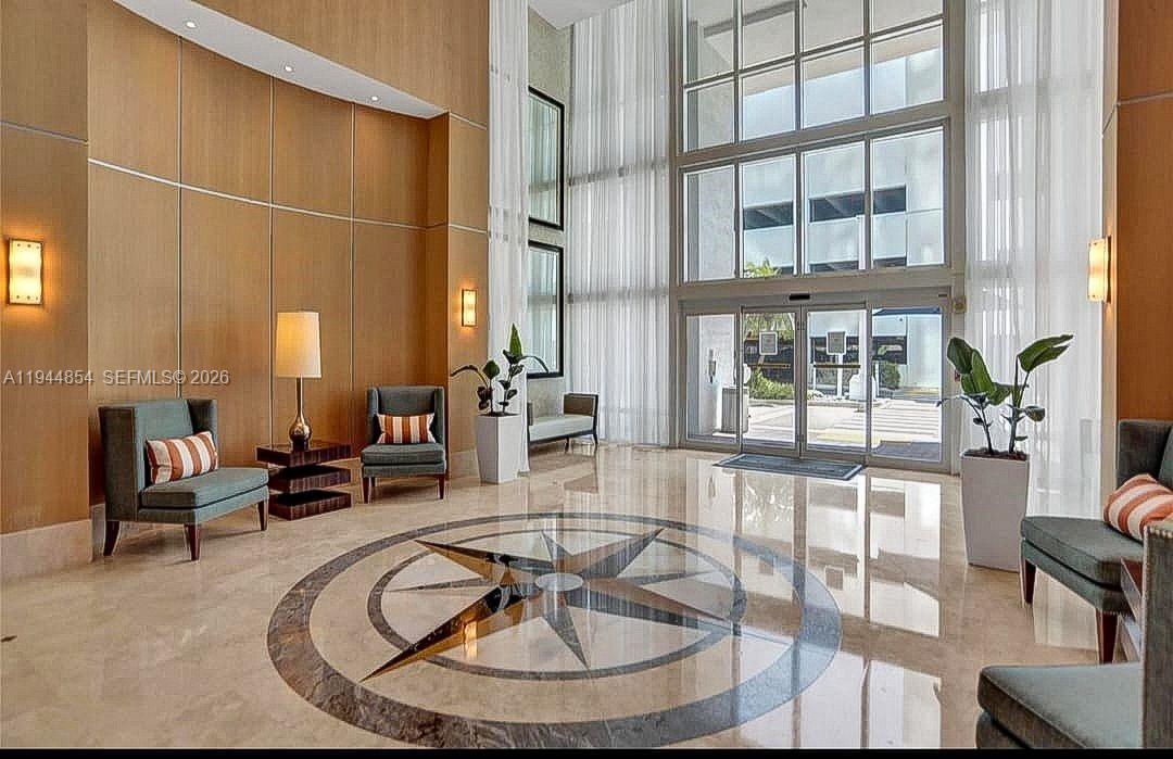 A modern lobby features a compass rose floor inlay, floor-to-ceiling windows, and seating areas — 1945 S Ocean Dr # 1405, Hallandale Beach FL 33009, HALLANDALE BEACH, FL