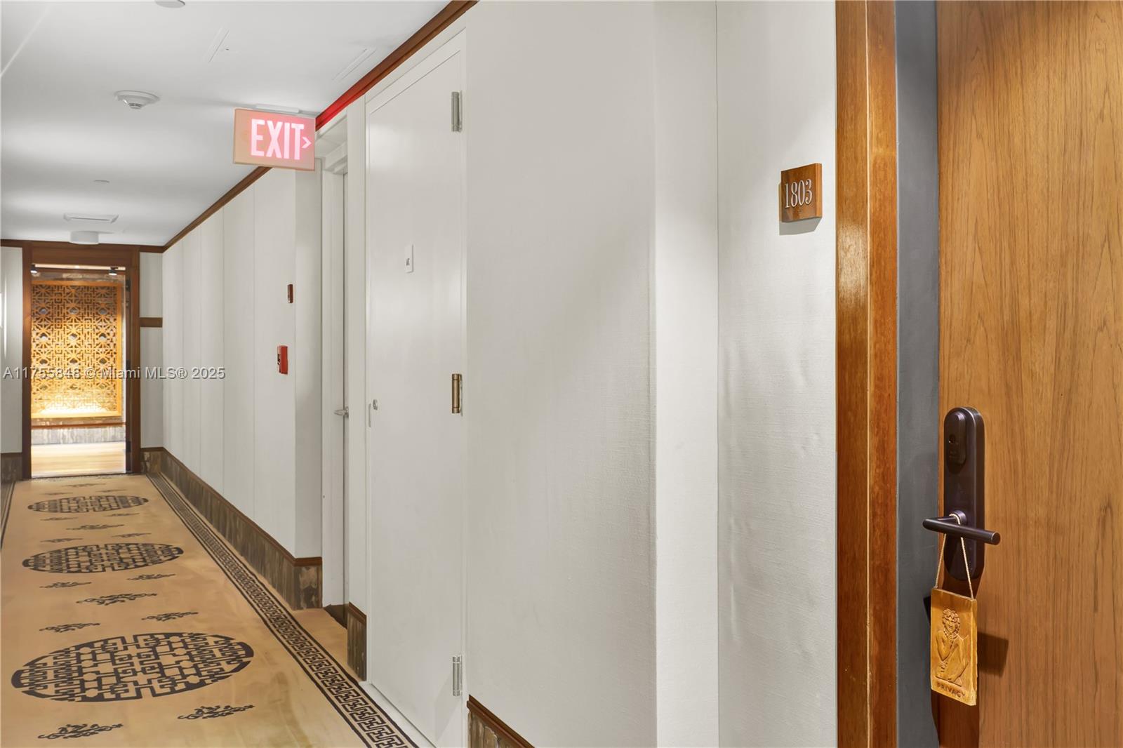 A hotel hallway features a patterned carpet, white walls, and a wooden door labeled 1803 — 101 20, Miami Beach FL 33139, MIAMI BEACH, FL