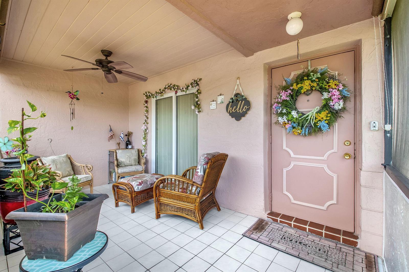 A covered patio features tiled flooring, wicker furniture, a pink door, and a floral wreath — 14195 Campanelli Drive, Delray Beach FL 33484, DELRAY BEACH, FL
