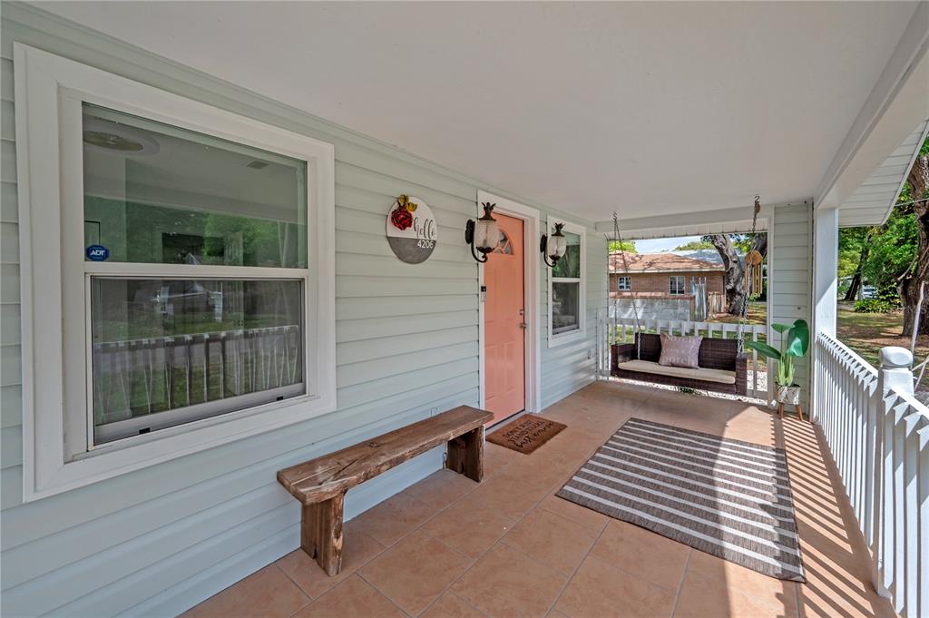 A covered front porch features light blue siding, a peach door, a bench, and a swing — 4206 N DOWNING AVENUE, TAMPA, FL