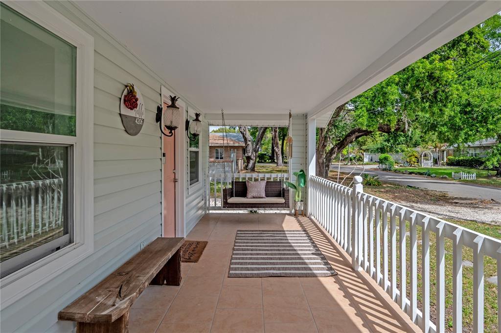 A covered porch features a wooden bench, a hanging swing, and a striped area rug — 4206 N DOWNING AVENUE, TAMPA, FL