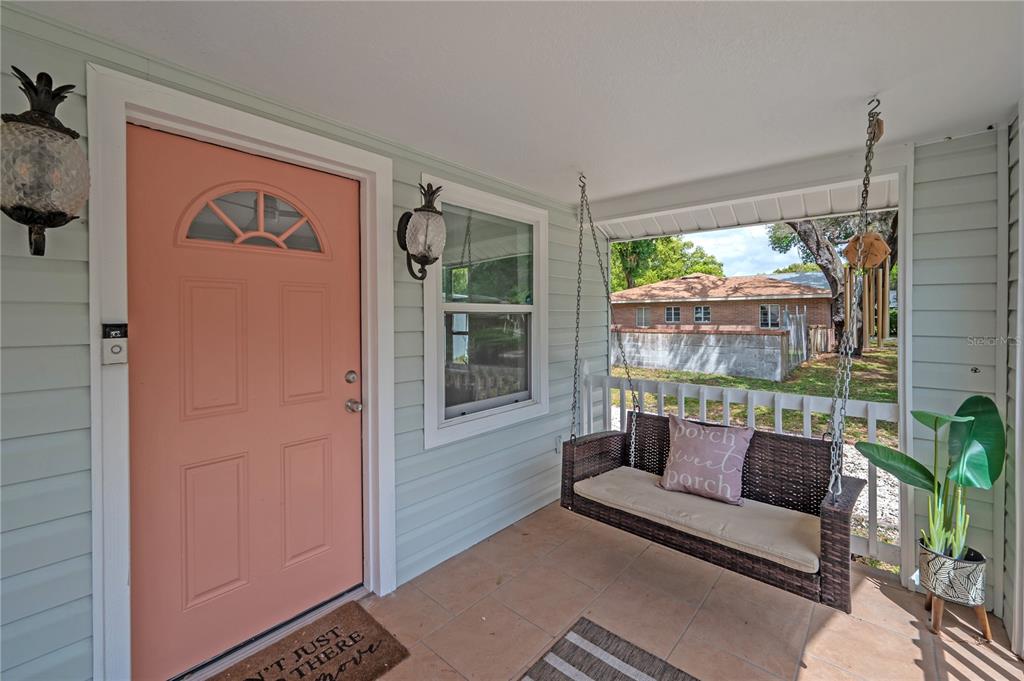 A covered front porch features a peach door, a hanging swing, and light blue siding — 4206 N DOWNING AVENUE, TAMPA, FL