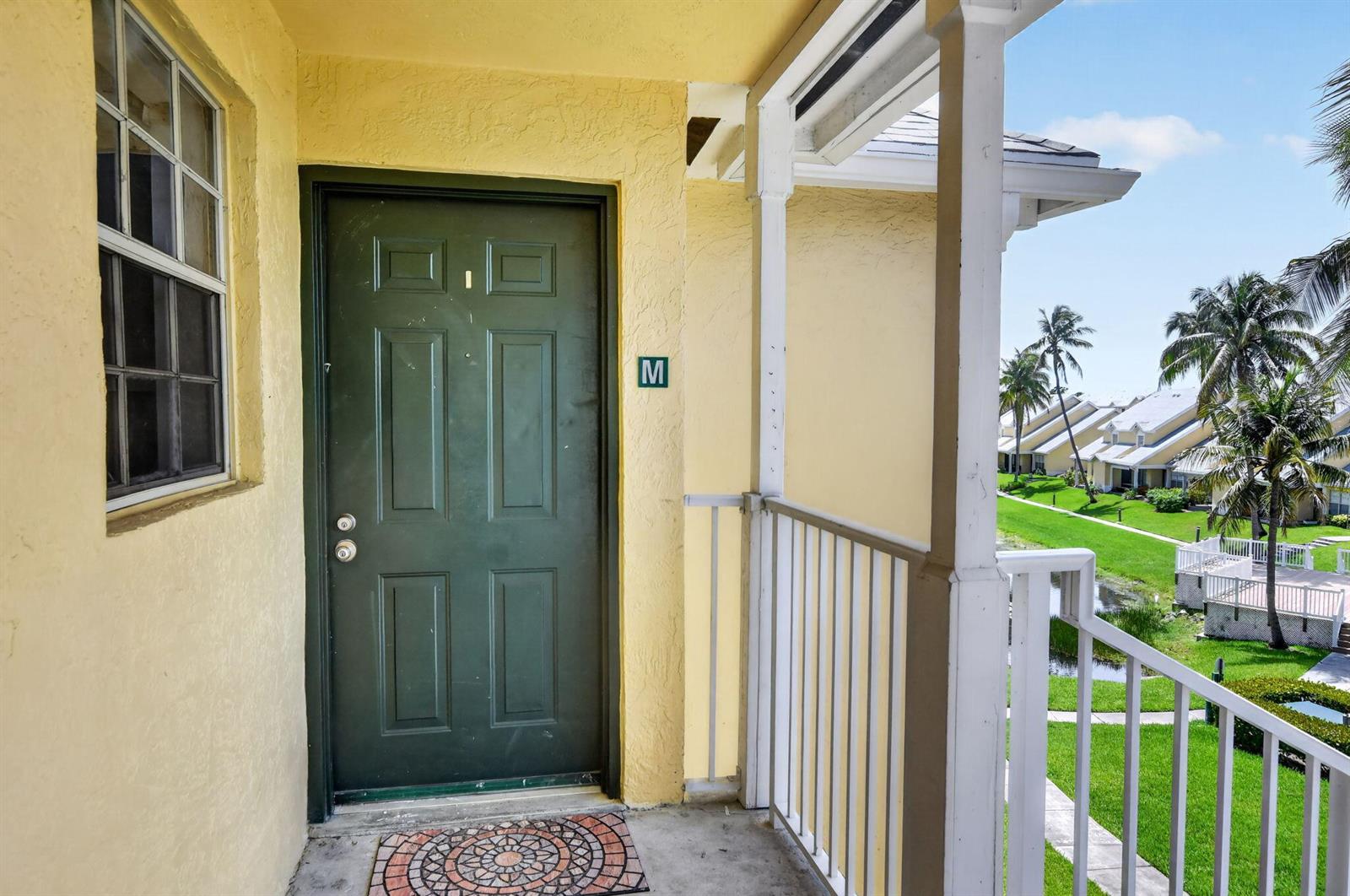 A dark green front door with a letter M sign on a yellow exterior balcony — 6323 La Costa Drive # M, Boca Raton FL 33433, BOCA RATON, FL