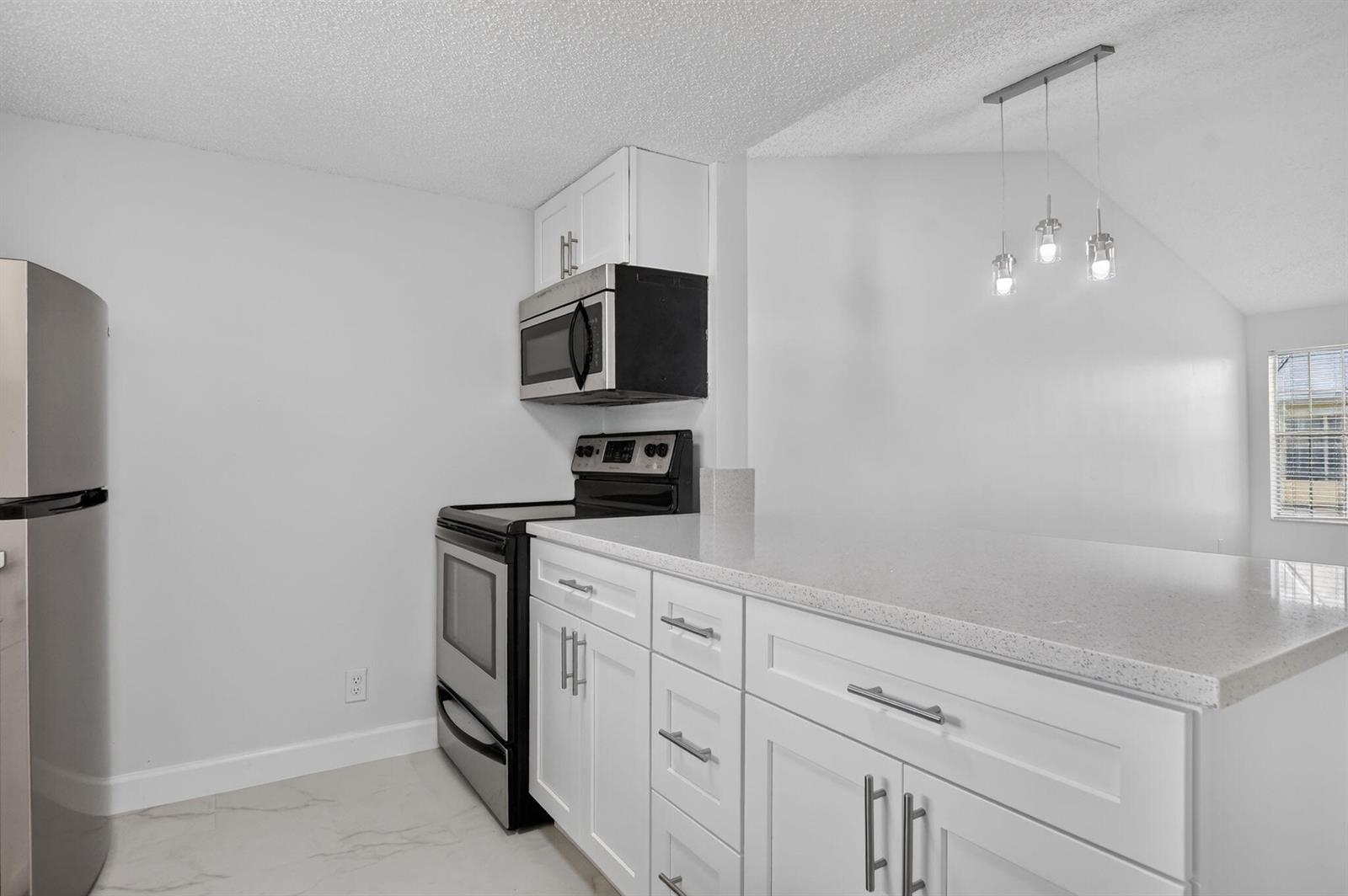 A kitchen features white cabinets, a quartz countertop, stainless steel appliances, and pendant lighting — 6323 La Costa Drive # M, Boca Raton FL 33433, BOCA RATON, FL