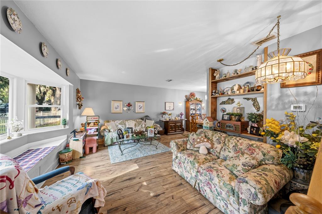 A living room features floral sofas, wood-look flooring, a bay window, and open shelving — 11690 SE 132ND STREET ROAD, OCKLAWAHA, FL