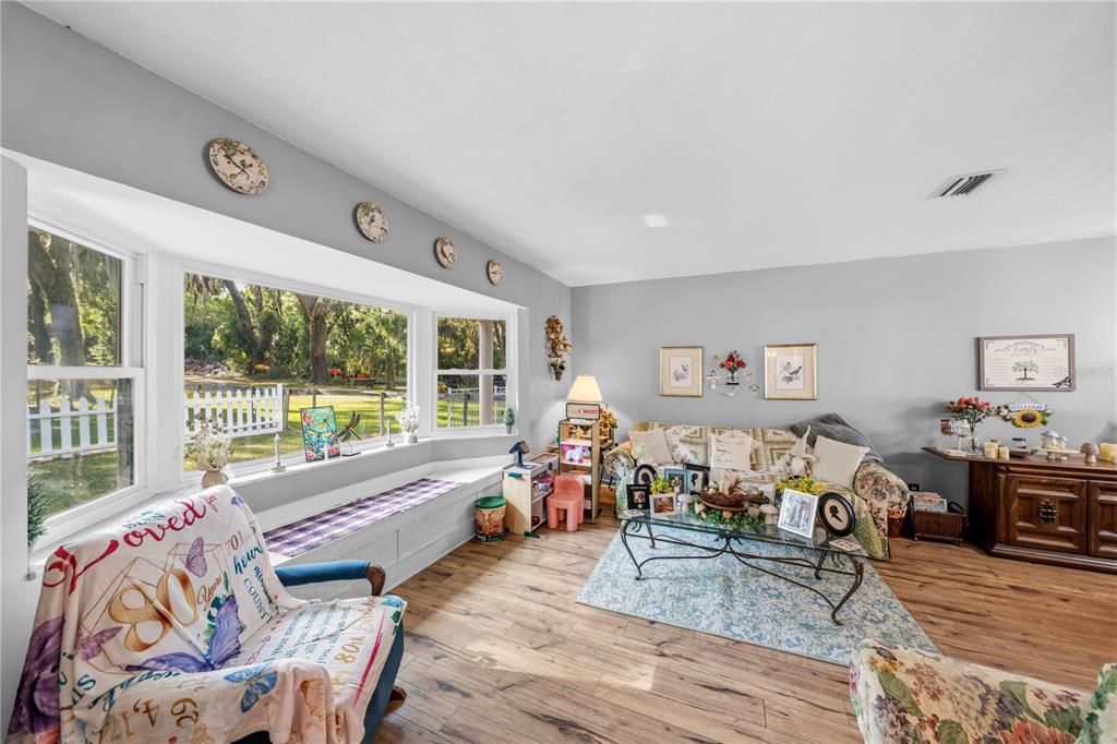 A living room features a bay window with a bench seat and wood-look flooring — 11690 SE 132ND STREET ROAD, OCKLAWAHA, FL