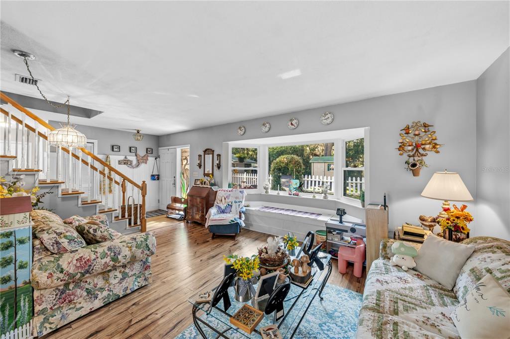 A living room features floral sofas, a bay window with a seat, and wood flooring — 11690 SE 132ND STREET ROAD, OCKLAWAHA, FL
