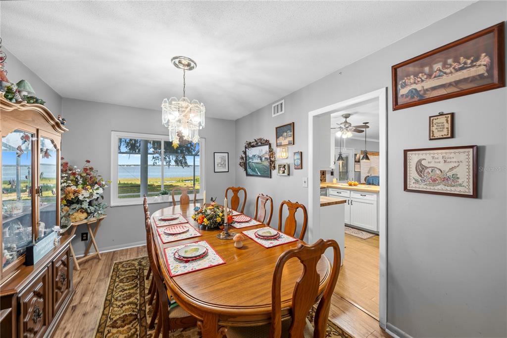 A dining room features a wooden table, chandelier, and a large window overlooking a lake — 11690 SE 132ND STREET ROAD, OCKLAWAHA, FL