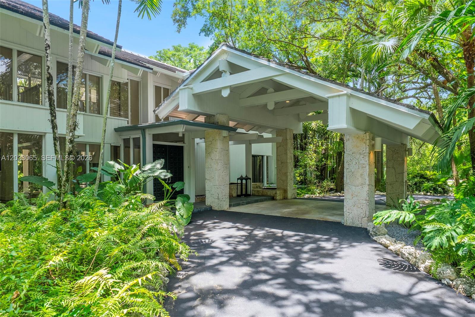 A large house with a stone-pillared porte-cochère and lush tropical landscaping in the foreground — 5600 Oakwood Ln, Coral Gables FL 33156, CORAL GABLES, FL