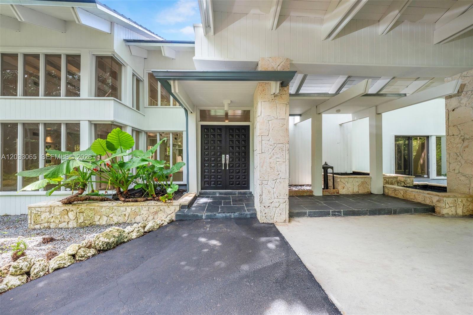 The exterior of a modern house features a stone-clad entryway with double doors and landscaping — 5600 Oakwood Ln, Coral Gables FL 33156, CORAL GABLES, FL