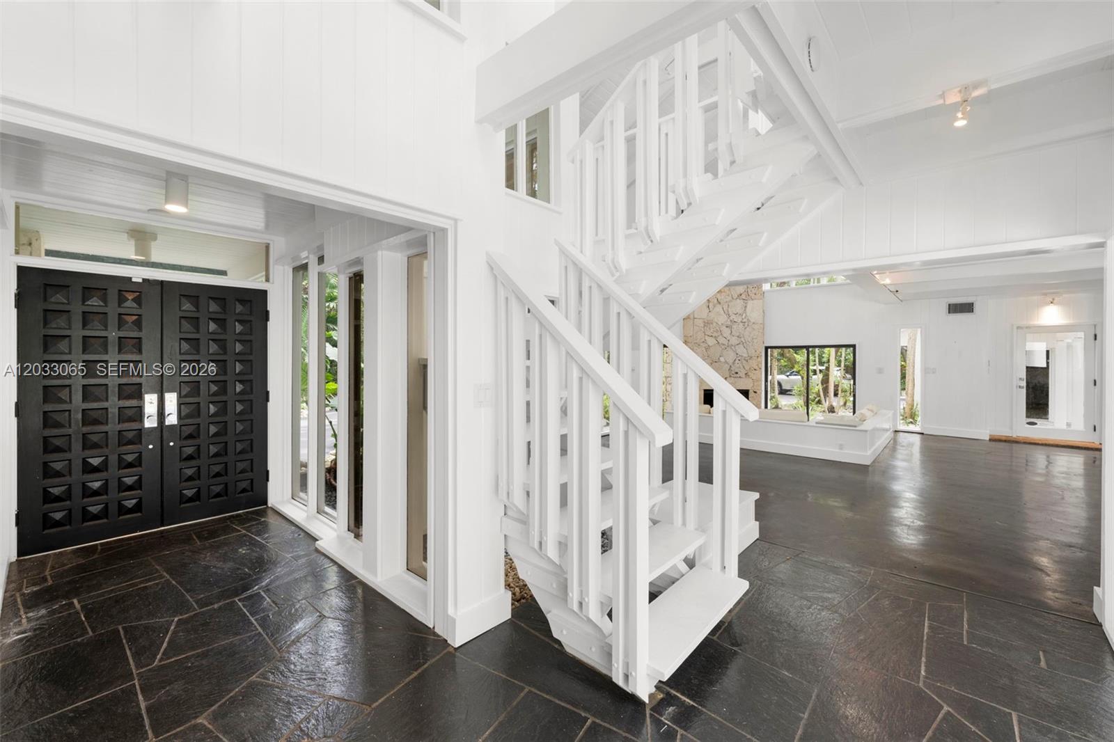 A white staircase stands in an entryway with black stone flooring and a black door — 5600 Oakwood Ln, Coral Gables FL 33156, CORAL GABLES, FL