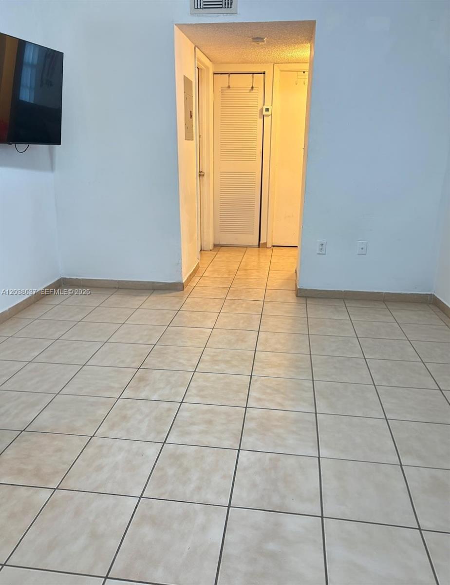A room with light-colored tile flooring leads to a hallway with two closed doors — 2560 W 60th St # 104, Hialeah FL 33016, HIALEAH, FL