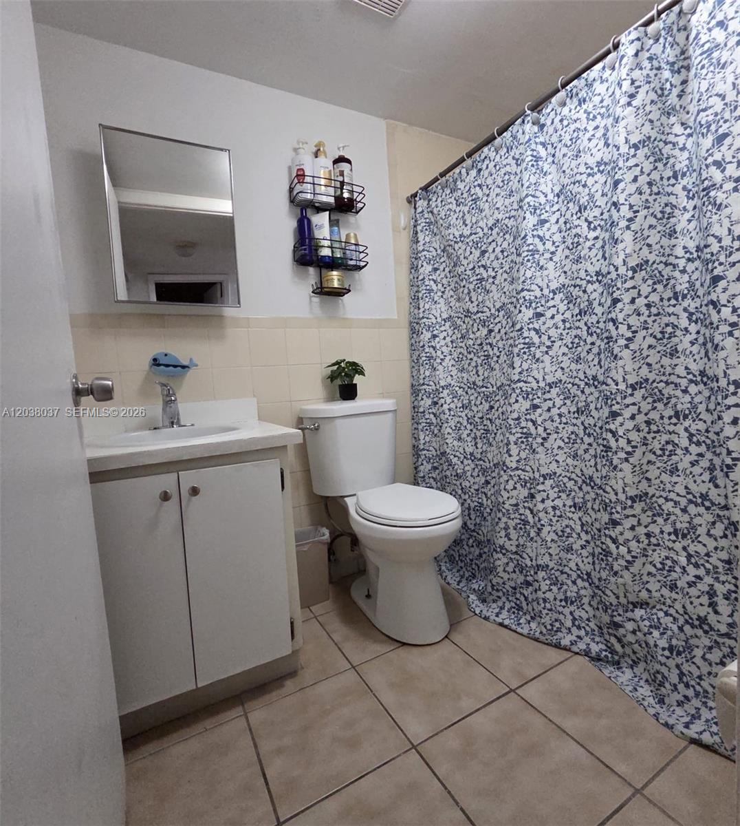 A bathroom features a vanity, toilet, wall-mounted storage rack, and a blue patterned shower curtain — 2560 W 60th St # 104, Hialeah FL 33016, HIALEAH, FL