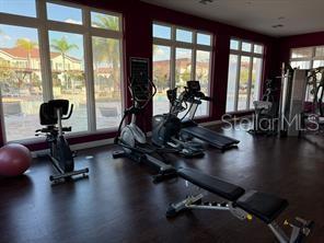 A fitness center features exercise equipment, dark wood flooring, and large windows overlooking a pool — 8962 SILVER PLACE, KISSIMMEE, FL