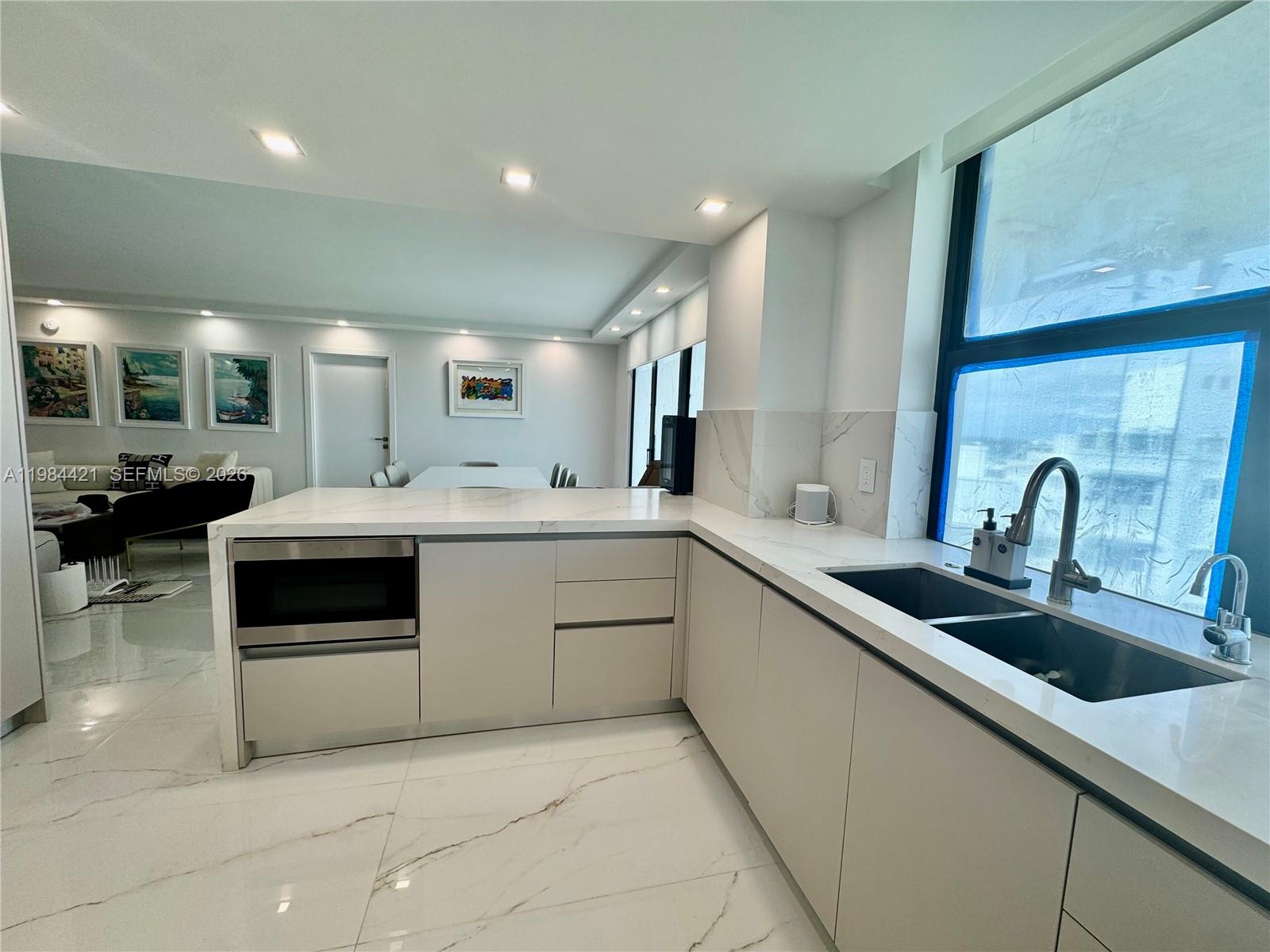 A modern kitchen features white marble countertops, light cabinetry, and a large window — 9801 Collins Ave # 20E, Bal Harbour FL 33154, BAL HARBOUR, FL