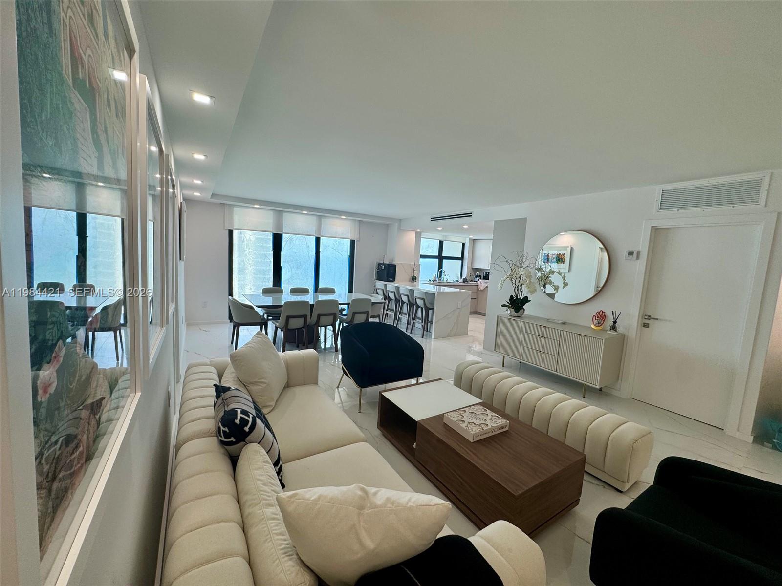 A modern living and dining area features white tile floors, neutral furniture, and a kitchen — 9801 Collins Ave # 20E, Bal Harbour FL 33154, BAL HARBOUR, FL