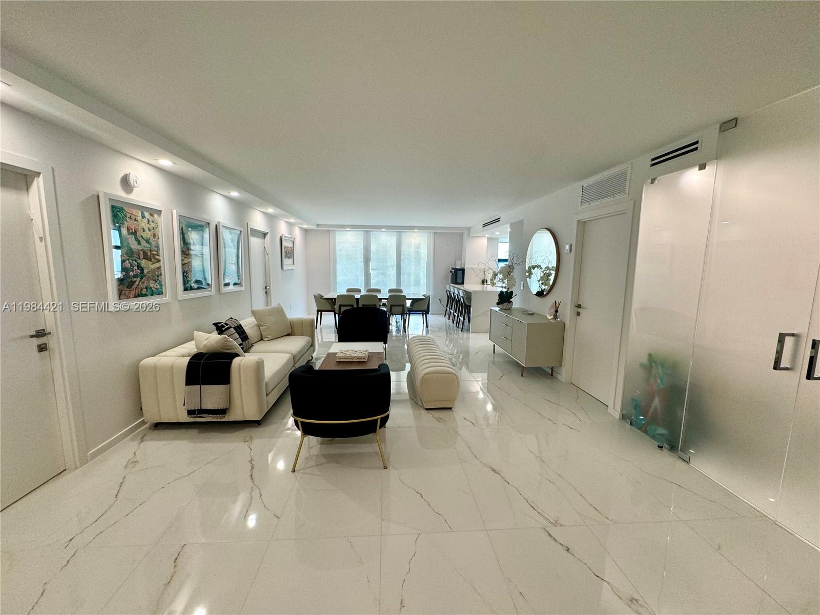 A modern living and dining area features white marble floors, neutral furniture, and recessed lighting — 9801 Collins Ave # 20E, Bal Harbour FL 33154, BAL HARBOUR, FL