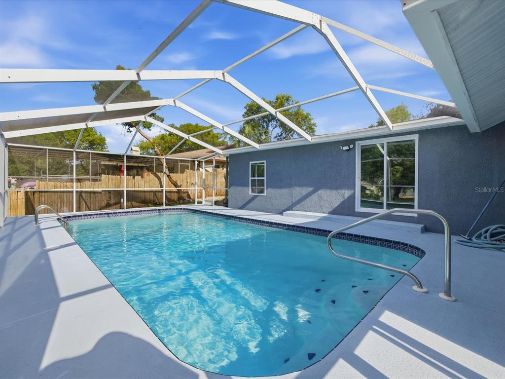 A swimming pool with a screen enclosure sits on a concrete patio beside a house — 6063 AIRMONT DRIVE, SPRING HILL, FL