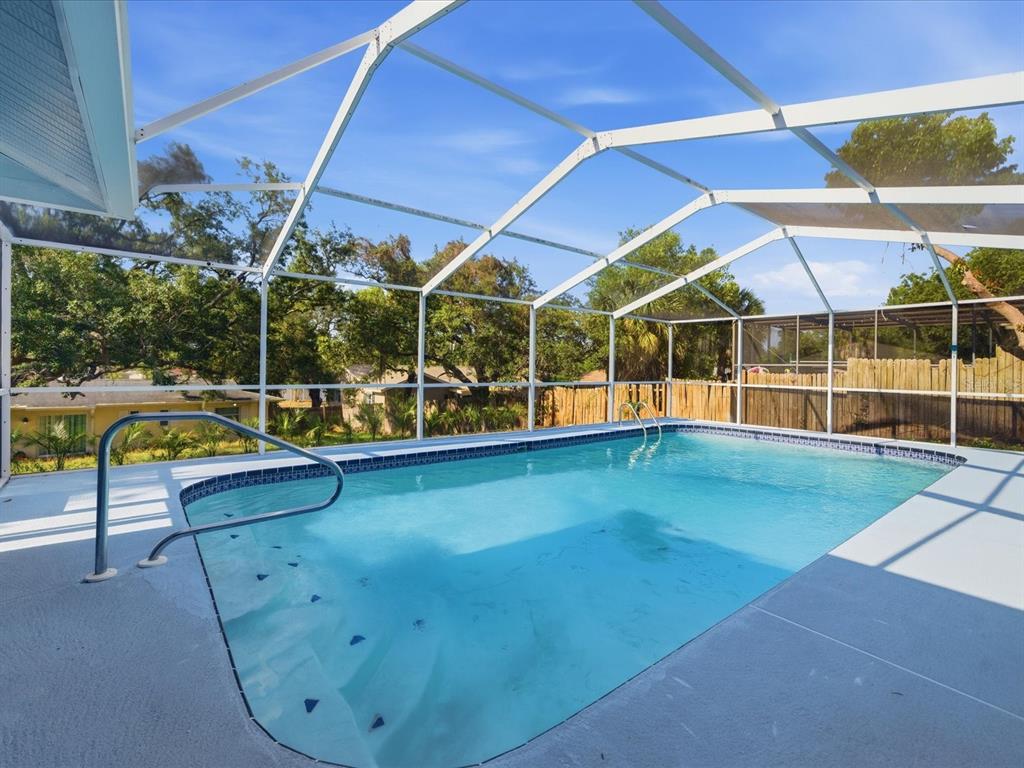 A swimming pool with a screen enclosure and a metal handrail on a concrete deck — 6063 AIRMONT DRIVE, SPRING HILL, FL