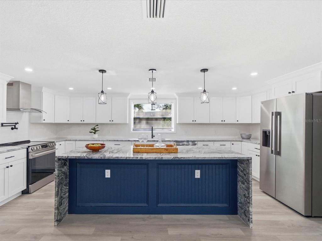 A modern kitchen features white cabinets, a blue island with a stone countertop, and stainless appliances — 6063 AIRMONT DRIVE, SPRING HILL, FL