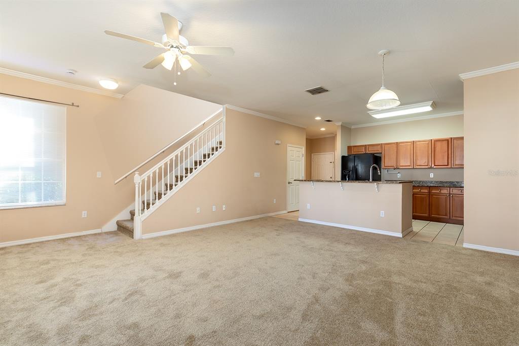 A carpeted living room features a staircase with white railings and an open kitchen beyond — 2536 LANCIEN COURT UNIT 5, ORLANDO, FL