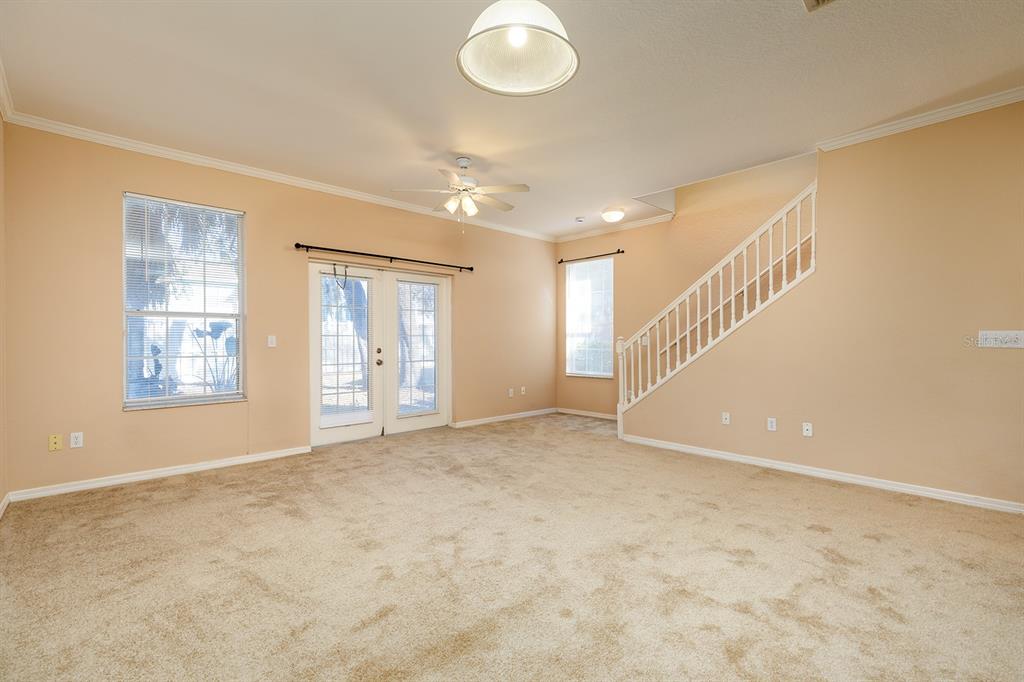 An empty living room features beige carpet, tan walls, a ceiling fan, and a staircase — 2536 LANCIEN COURT UNIT 5, ORLANDO, FL