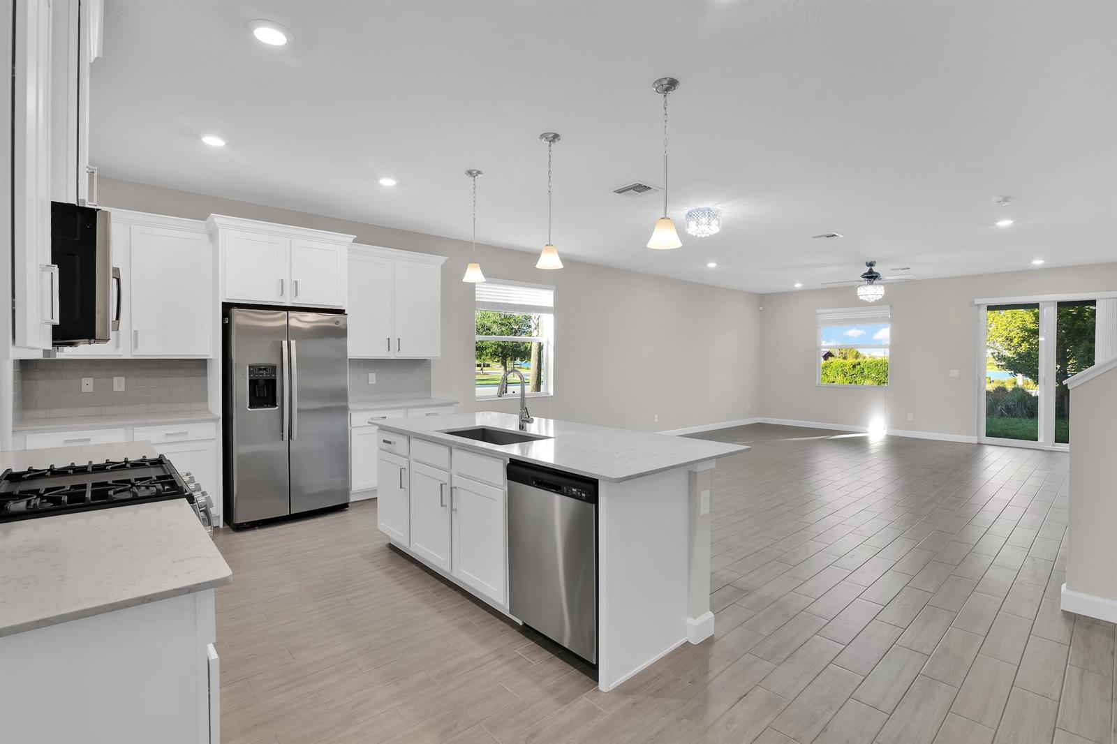 A modern kitchen with white cabinets, stainless steel appliances, and an island overlooks an open-concept living area — 1168 Sterling Pine Place, Loxahatchee FL 33470, LOXAHATCHEE, FL