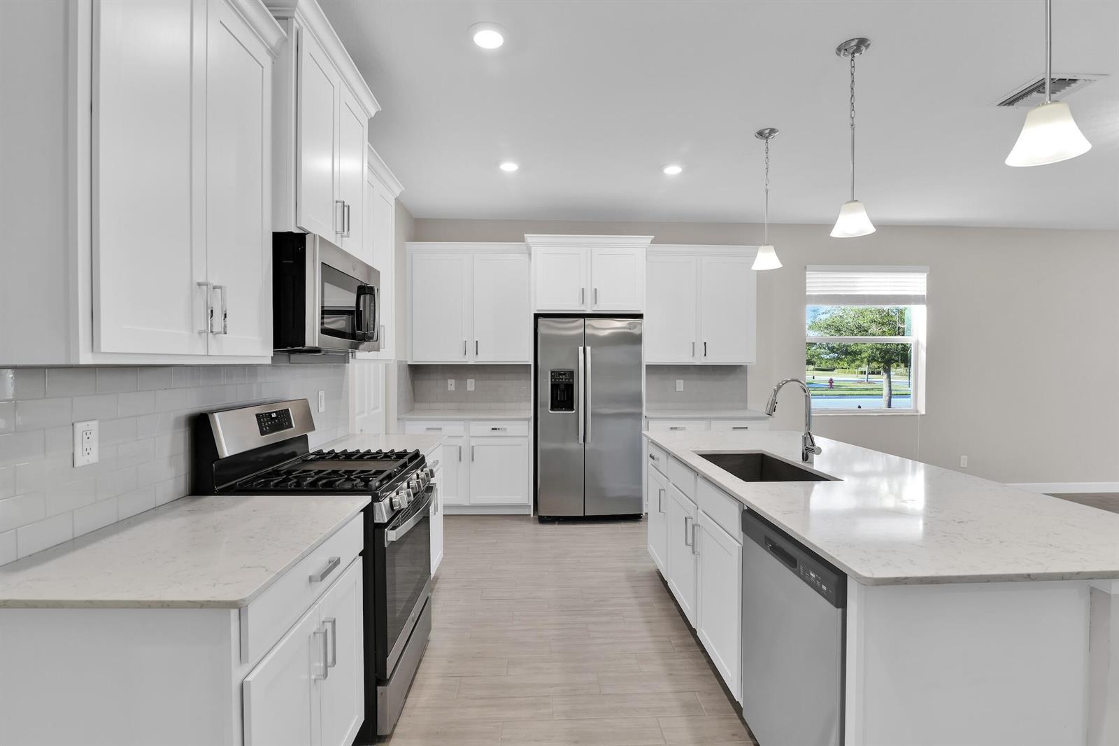 A modern kitchen features white cabinets, stainless steel appliances, quartz countertops, and a center island — 1168 Sterling Pine Place, Loxahatchee FL 33470, LOXAHATCHEE, FL