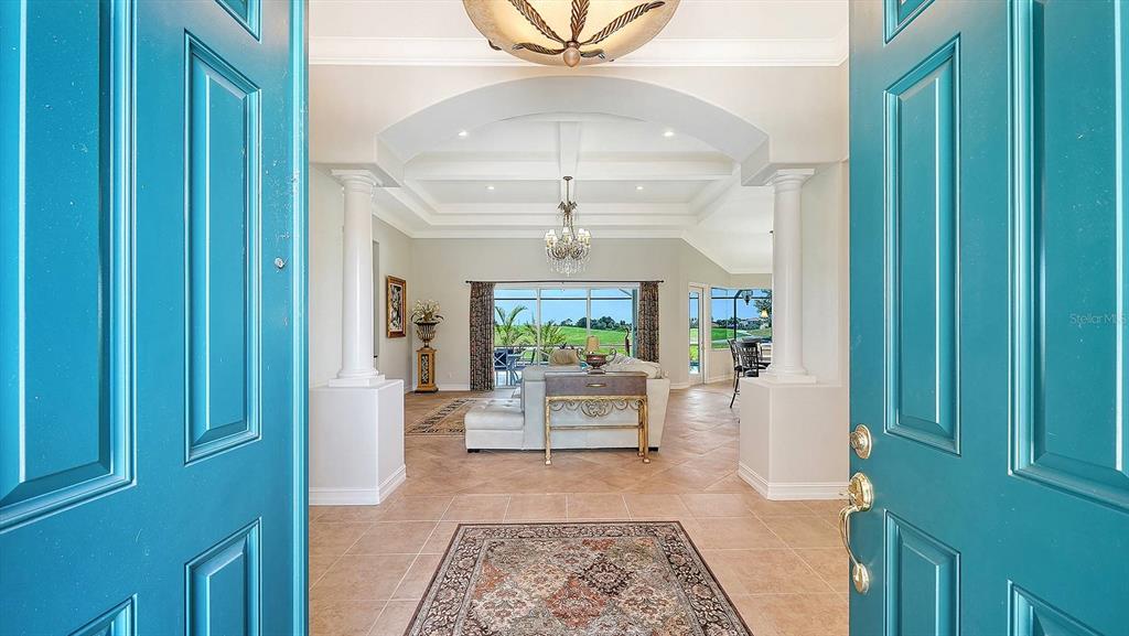 A view through an open teal door into a foyer with columns and a chandelier — 225 PESARO DRIVE, NORTH VENICE, FL