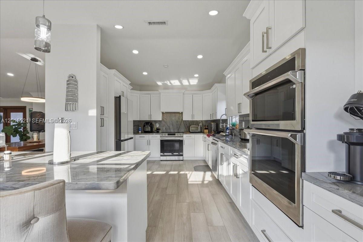 A modern kitchen features white cabinetry, stainless steel appliances, and a marble-topped island — 16540 SW 145th Ct, Miami FL 33177, MIAMI, FL