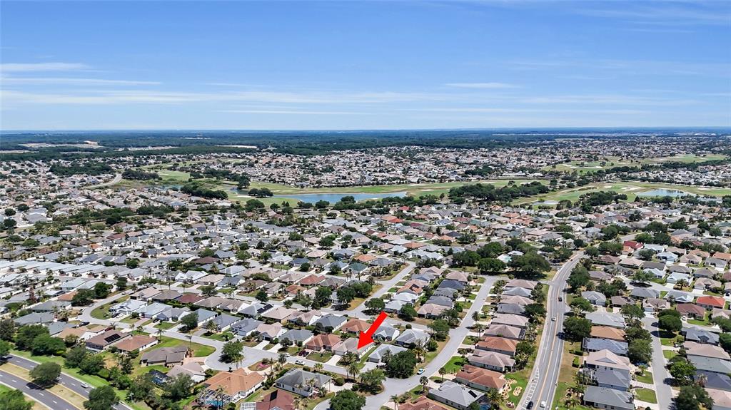 An aerial view shows a suburban neighborhood with a red arrow pointing to a house — 934 MOSES LOOP, THE VILLAGES, FL