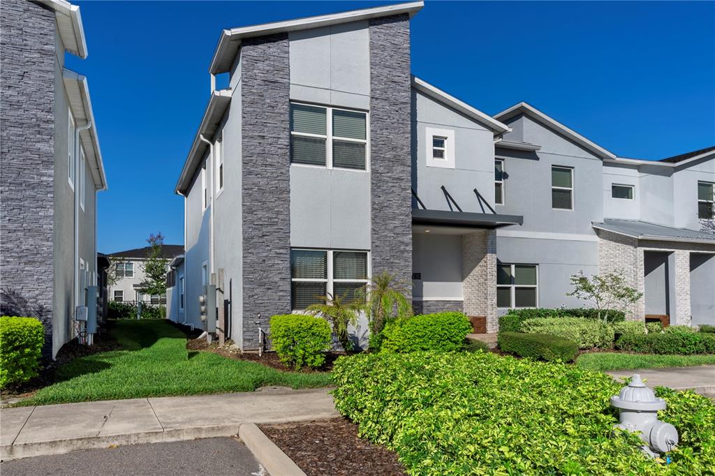 A two-story townhouse exterior features gray stucco walls, stone veneer accents, and a small porch — 230 OCEAN COURSE AVENUE, DAVENPORT, FL