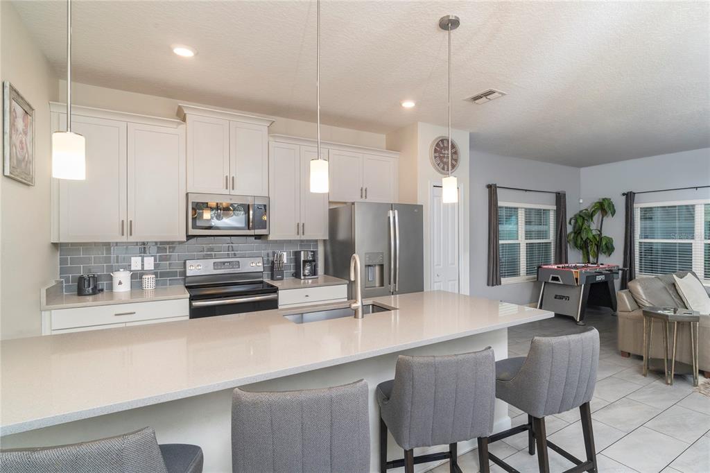 A kitchen features light cabinets, a quartz island with bar seating, and stainless steel appliances — 230 OCEAN COURSE AVENUE, DAVENPORT, FL