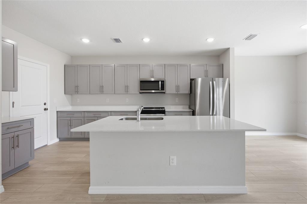 A modern kitchen features gray cabinets, white countertops, a central island, and stainless steel appliances — 37114 SAGEMOOR DRIVE, ZEPHYRHILLS, FL