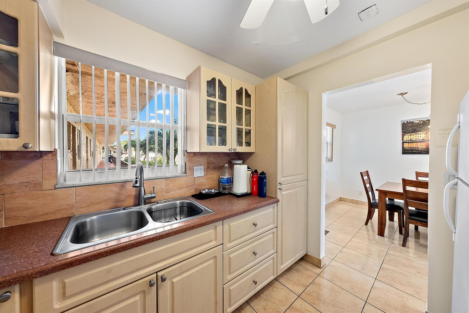 A kitchen with light wood cabinets, a double sink, and a view of an exterior walkway — 701 Lori Drive # 206, Palm Springs FL 33461, PALM SPRINGS, FL