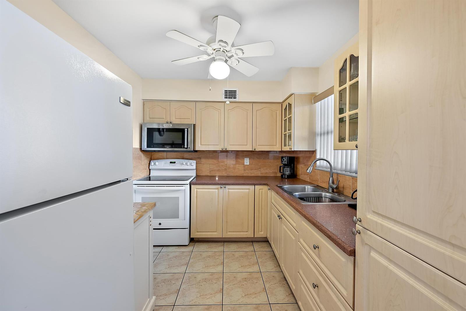 A kitchen features light wood cabinets, a white refrigerator, a white stove, and tiled flooring — 701 Lori Drive # 206, Palm Springs FL 33461, PALM SPRINGS, FL