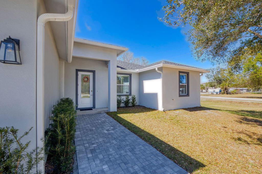 A paved walkway leads to the front entrance of a light-colored house with gray trim — 3573 NW 18th Avenue, Okeechobee FL 34972, OKEECHOBEE, FL