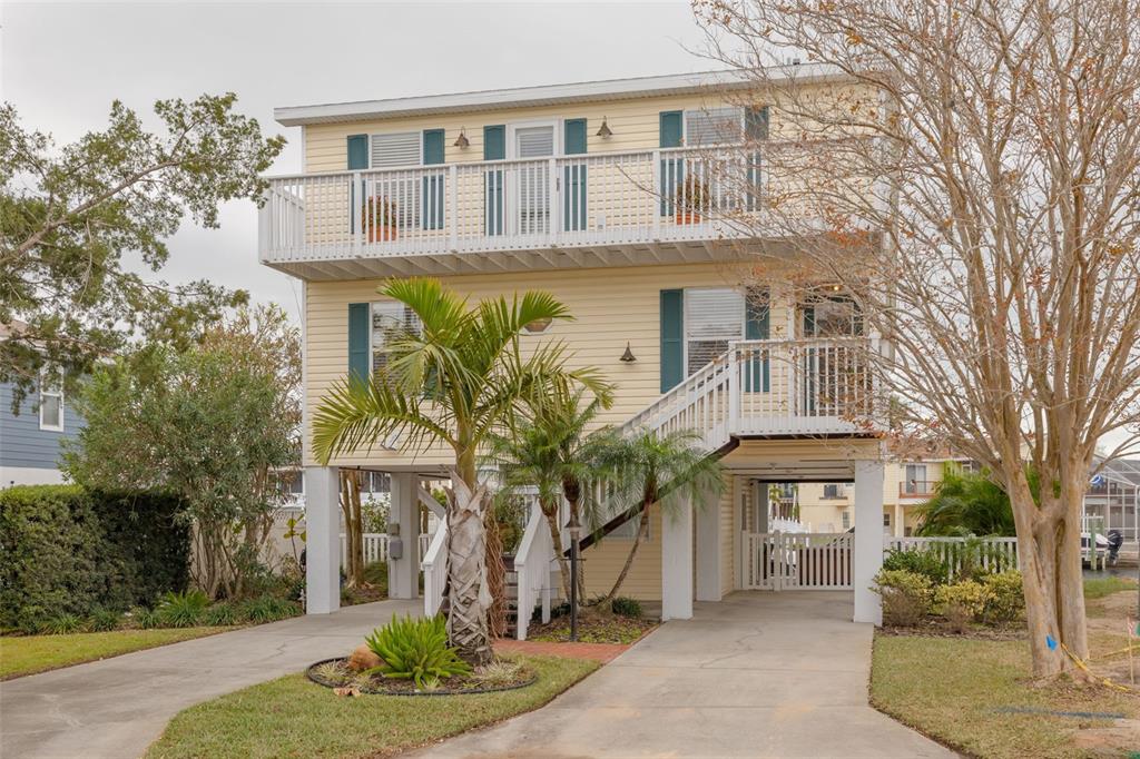 A three-story yellow house on stilts features a front staircase, balconies, and a concrete driveway — 4207 DES PREZ COURT, HERNANDO BEACH, FL