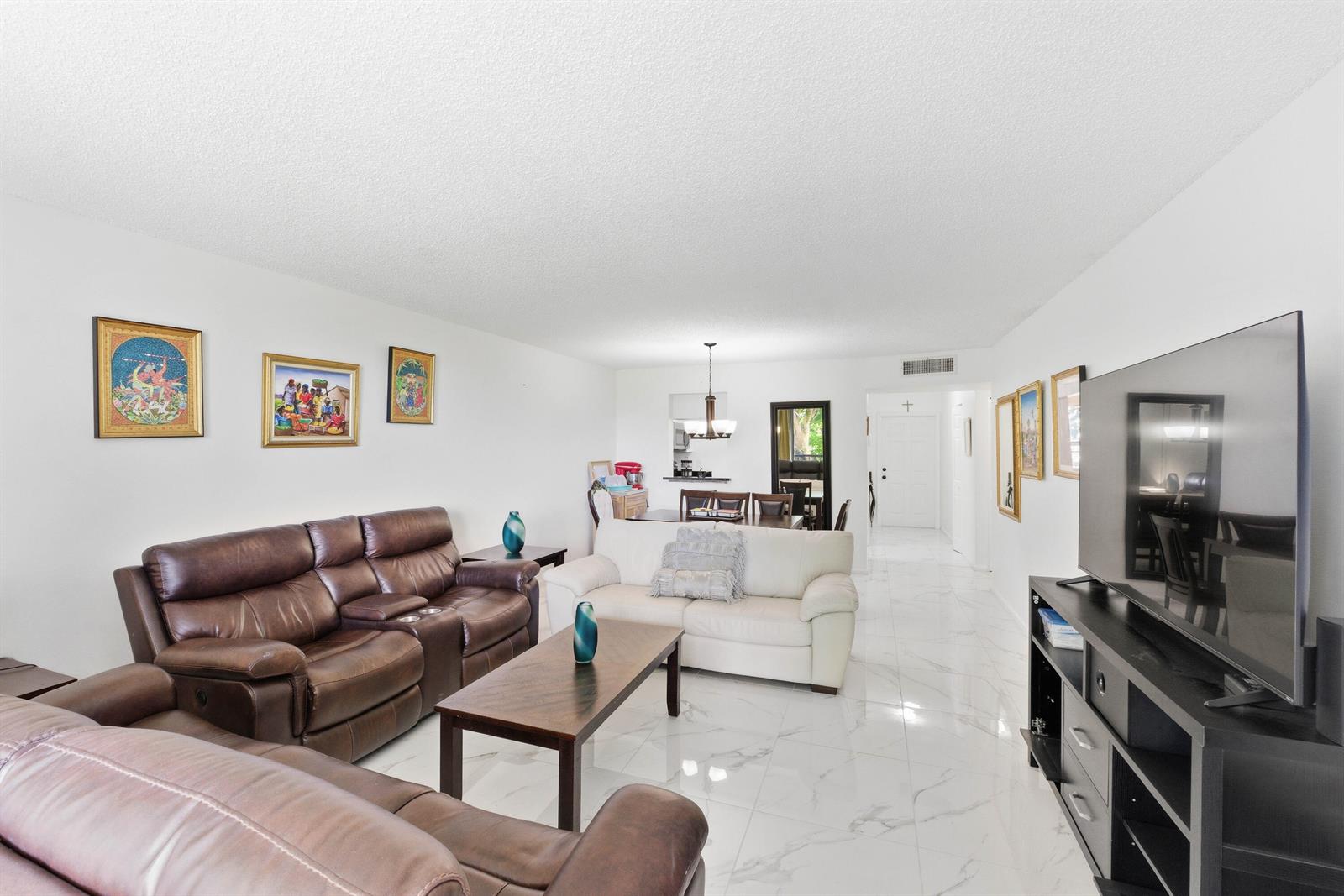 A living room features white walls, marble-look tile floors, leather sofas, and a television console — 260 NW 76th Avenue # 207, Margate FL 33063, MARGATE, FL