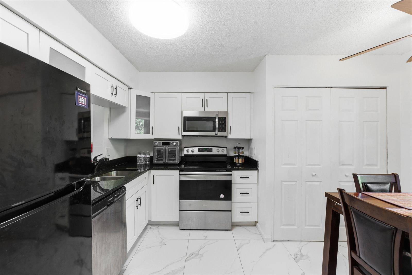 A kitchen features white cabinets, stainless steel appliances, black countertops, and white marble-patterned tile floors — 260 NW 76th Avenue # 207, Margate FL 33063, MARGATE, FL