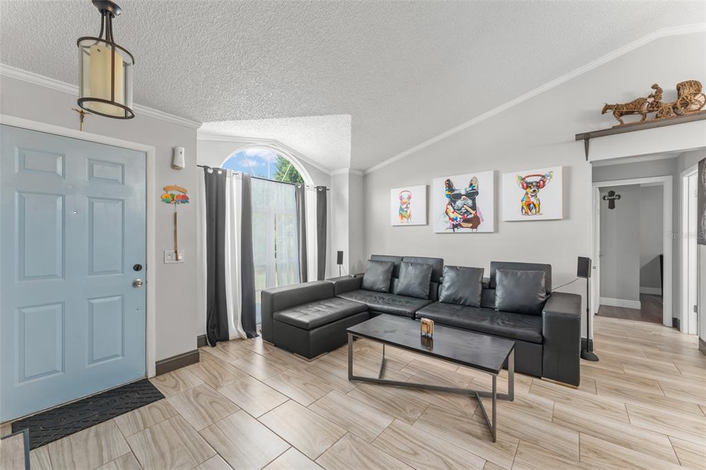 A living room features light wood-look tile floors, a black sectional sofa, and a blue door — 961 MILLENBECK AVENUE, DELTONA, FL