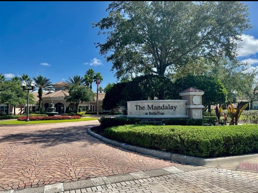 A stone monument sign for The Mandalay at BellaTrae sits beside a paved entrance road — 1357 VENEZIA COURT UNIT 102, DAVENPORT, FL