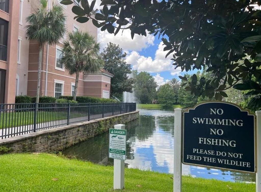 A pond with a fountain is situated next to a residential building and warning signs — 1357 VENEZIA COURT UNIT 102, DAVENPORT, FL