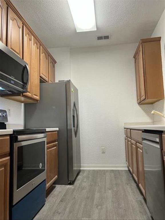 A galley-style kitchen features wood cabinets, stainless steel appliances, and light-colored flooring — 1357 VENEZIA COURT UNIT 102, DAVENPORT, FL
