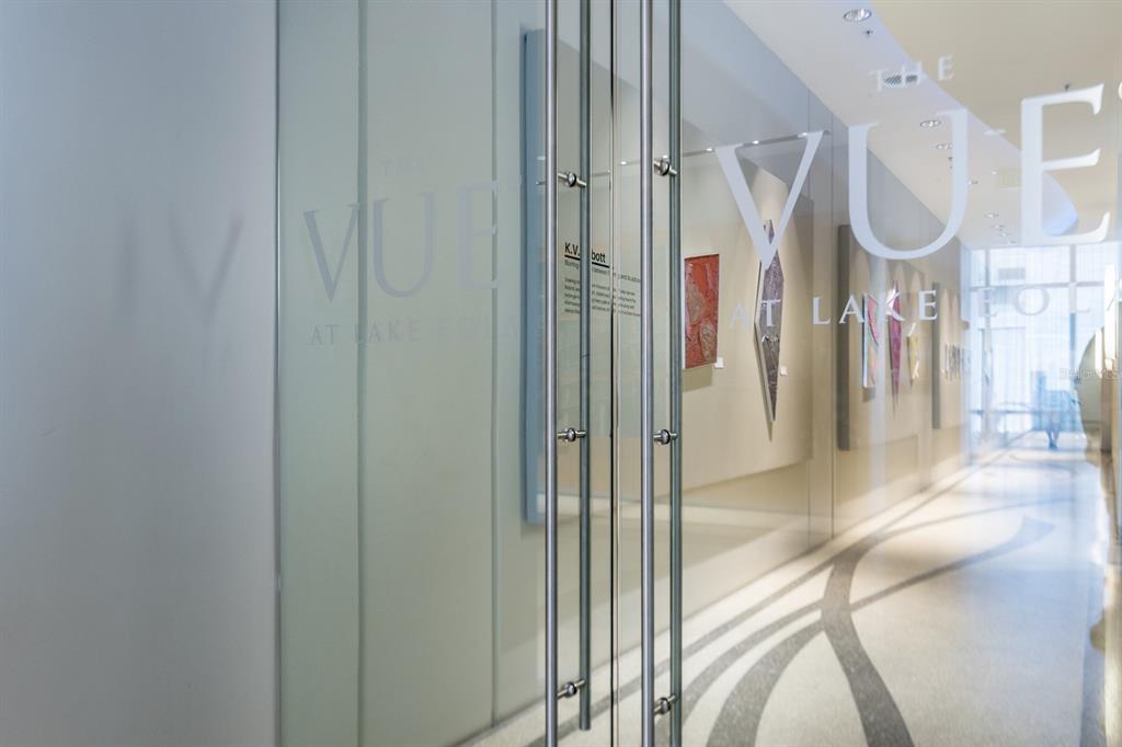 A glass door entrance leads into a hallway decorated with framed artwork and patterned flooring — 150 E ROBINSON STREET UNIT 1810, ORLANDO, FL